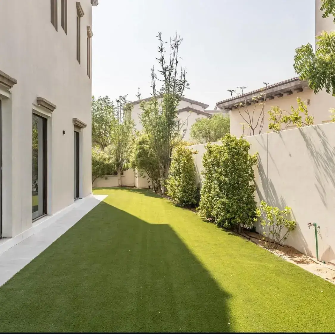 Minimalist villa Contemporary garden in Dubai featuring realistic artificial grass with a flawless green finish, bordered by white rendered villa walls and structured planting of lush shrubs and young trees — a low-maintenance modern outdoor space by British-owned Reshape Landscaping Dubai. in Dubai featuring artificial grass and clean modern boundaries. Designed by Reshape Landscaping and Design, a British-owned landscaping company in Dubai creating functional outdoor spaces with low-maintenance materials and contemporary styling.
