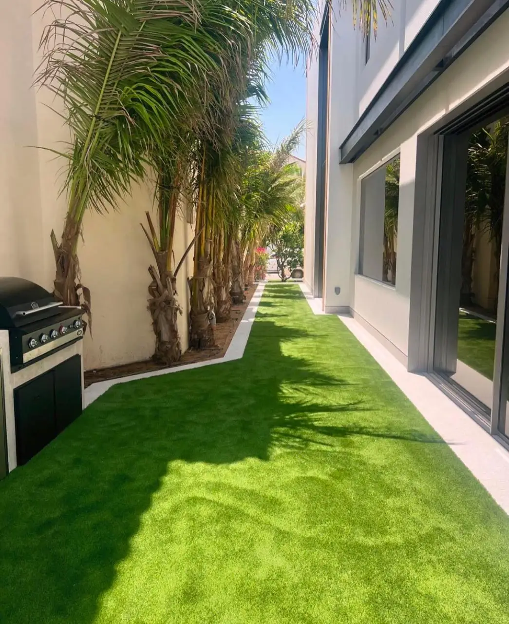Artificial grass installation in Dubai villa side garden with palm tree planting and low maintenance landscaping